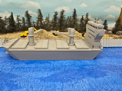 Model of a large ship on a blue surface with trees and construction vehicles in the background