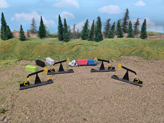 Model oil pumps and a truck on a sandy surface with trees in the background