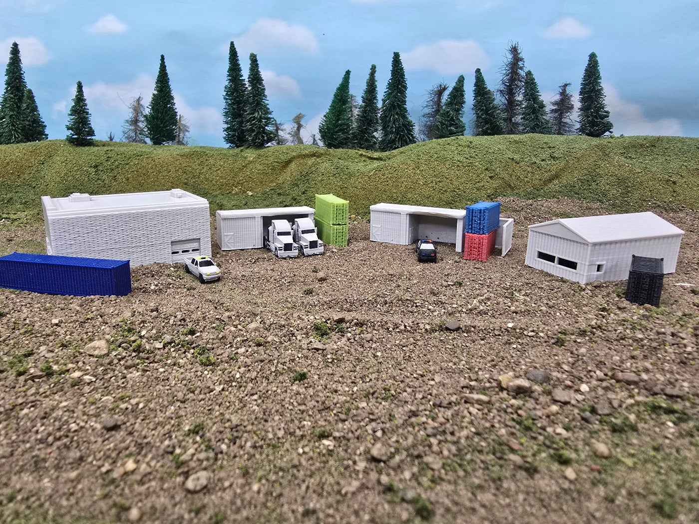 Model of a small town with buildings and vehicles on a textured surface with trees in the background.