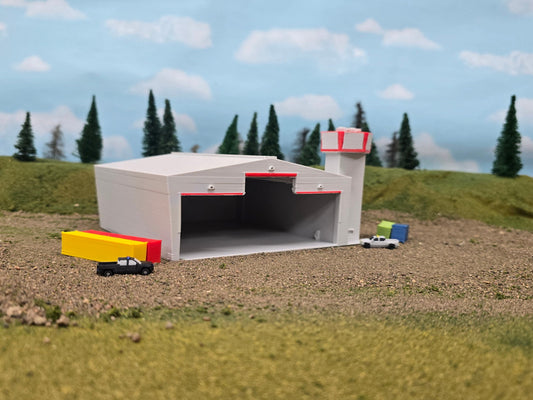 Model of a large industrial building with a truck in front, set against a scenic background with trees and sky.