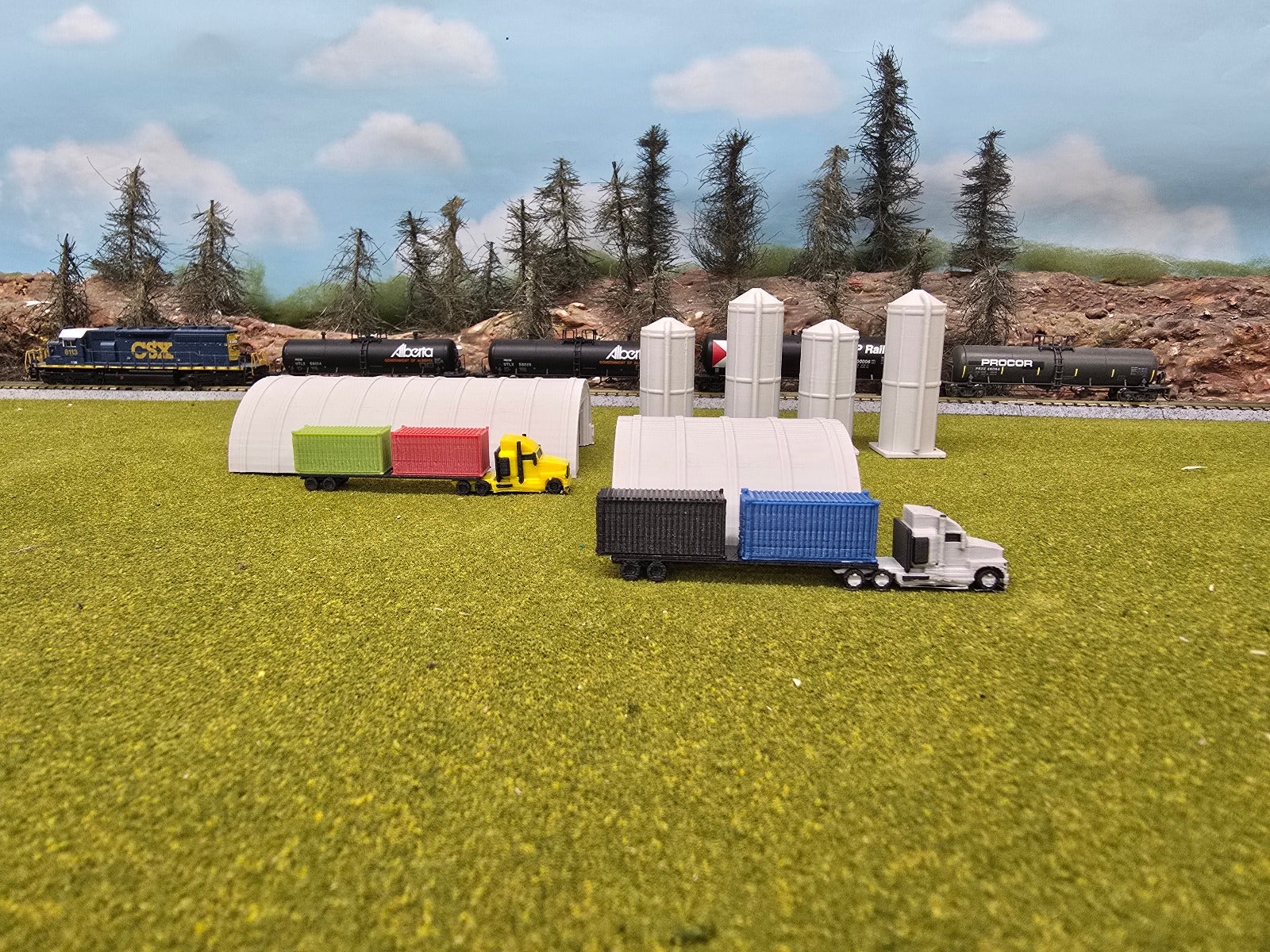 Model trains and trucks on a grassy field with trees in the background