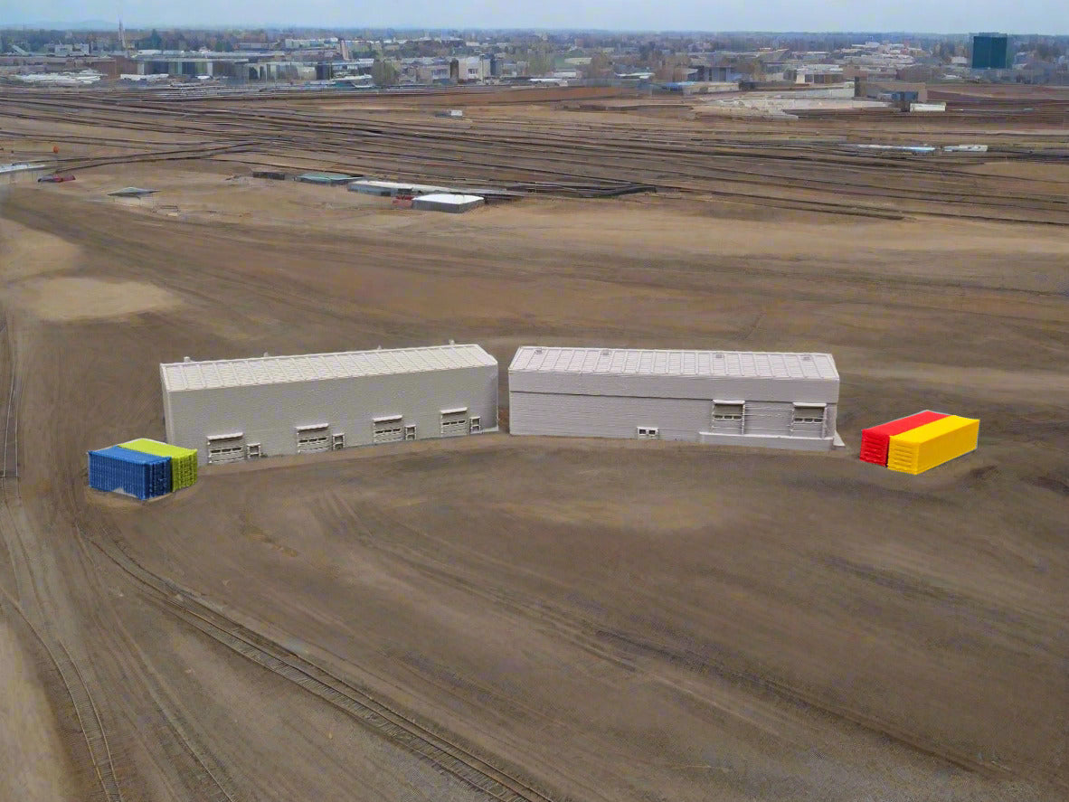 Model of two gray buildings with colorful containers on a model landscape with trees and sky.